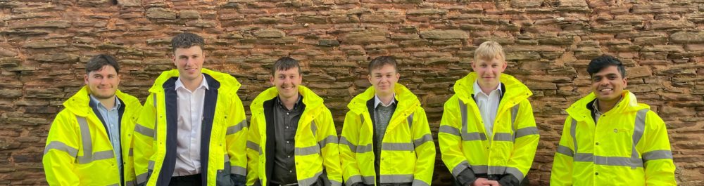 Group of surveyors wearing PPE standing in front of a wall.